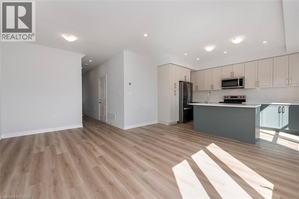 Open concept living area and kitchen with light wood flooring, white walls, and stainless steel appliances. - 205 Thames Way Unit# 12, Mount Hope