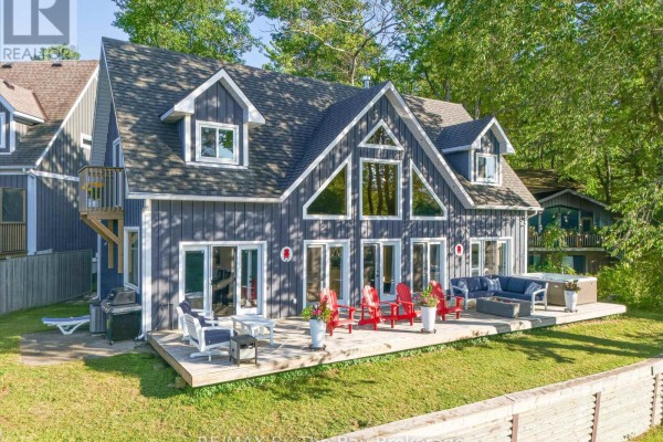 Rear exterior of dark blue house with expansive wooden deck overlooking water. - 2056 River Road W, Wasaga Beach