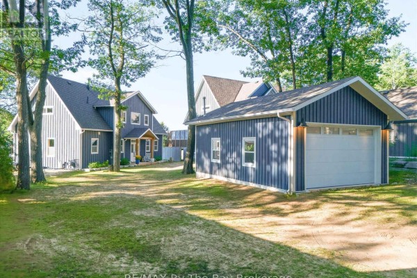 View of dark blue house and detached garage on a grassy lot. - 2056 River Road W, Wasaga Beach