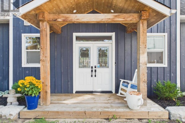 Front porch with double white doors, wooden beams, and rocking chair. - 2056 River Road W, Wasaga Beach