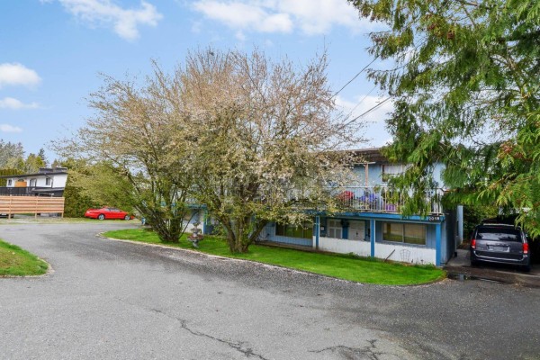 Side view of the light blue duplex, showing the upper balcony, carport, and surrounding grass. - 2058-2060 156 Street, Surrey