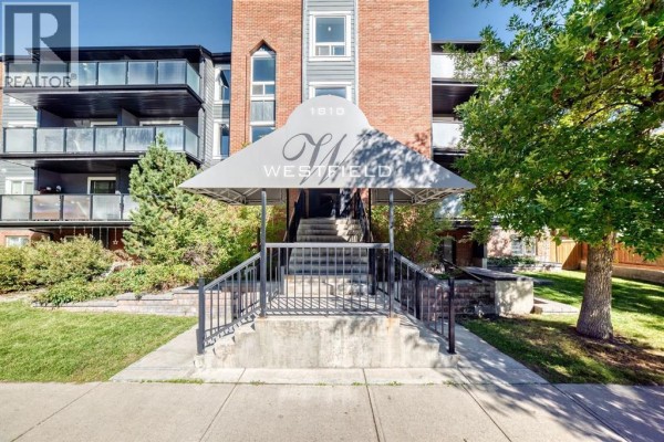 Covered entrance to apartment building with stairs, railings, and building name "Westfield". - 206, 1810 11 Avenue Sw, Calgary