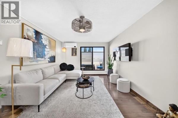 Living room with large sectional sofa, coffee table, fan, and city view from window. - 206, 1810 11 Avenue Sw, Calgary