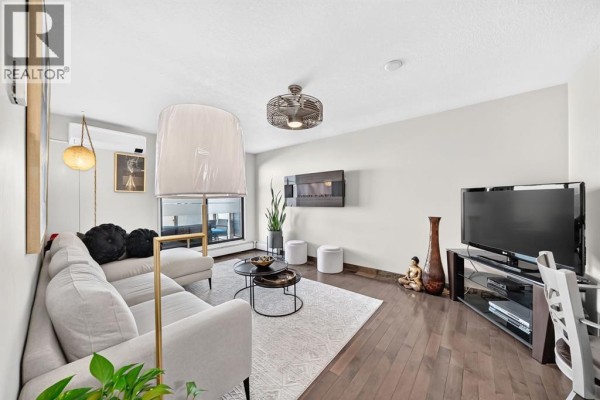 Living room with sectional sofa, coffee table, fireplace, TV, and dark wood floors. - 206, 1810 11 Avenue Sw, Calgary