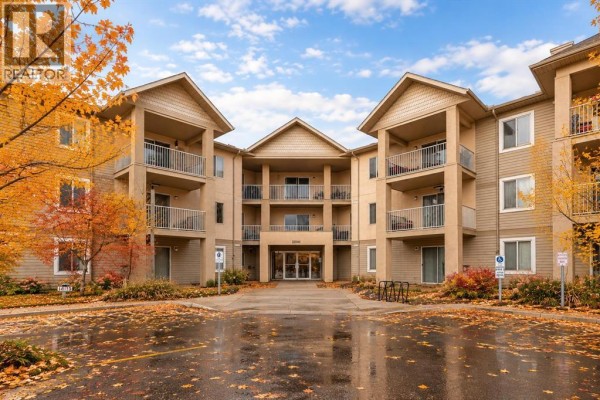 Exterior view of a beige apartment building with balconies and an entrance in the fall. - 206, 2000 Citadel Meadow Point Nw, Calgary