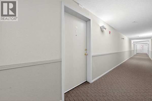 Interior hallway with beige carpet, textured walls, and doors leading to apartments. - 206, 2000 Citadel Meadow Point Nw, Calgary