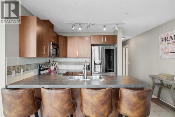 Kitchen with dark wood cabinets, stainless steel appliances, and island with sink. - 206, 210 15 Avenue Se, Calgary