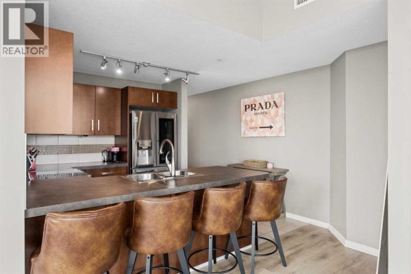 Kitchen with island, bar stools, dark wood cabinets, and stainless steel refrigerator. - 206, 210 15 Avenue Se, Calgary