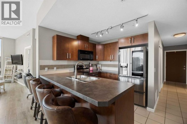 Kitchen with island seating, dark wood cabinets, and stainless steel appliances. - 206, 210 15 Avenue Se, Calgary