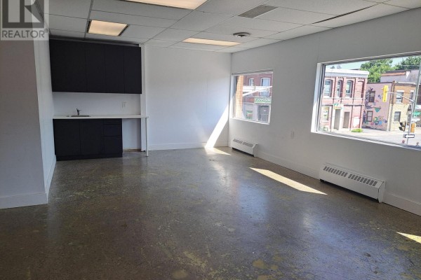 Empty commercial space with dark cabinets and sink on left, white walls, and windows. - 206 - 260 Dalhousie Street, Ottawa