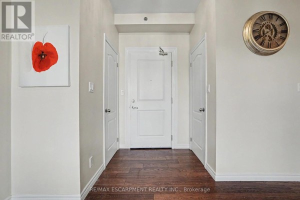 Apartment entrance with three doors, dark wood flooring, and a large decorative clock on the wall. - 206 - 34 Plains Road E, Burlington