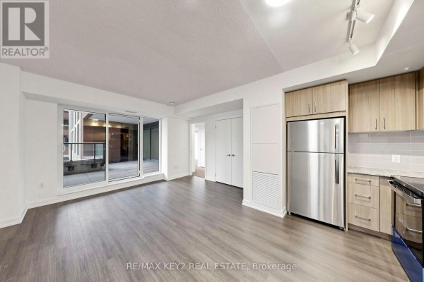 Open concept living area with gray wood-look flooring and a small kitchen with stainless steel appliances. - 206 - 4010 Eglinton Avenue W, Toronto