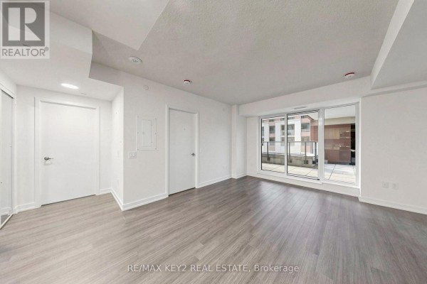 Living area with white walls, gray wood-look flooring, and glass sliding doors opening to a balcony. - 206 - 4010 Eglinton Avenue W, Toronto