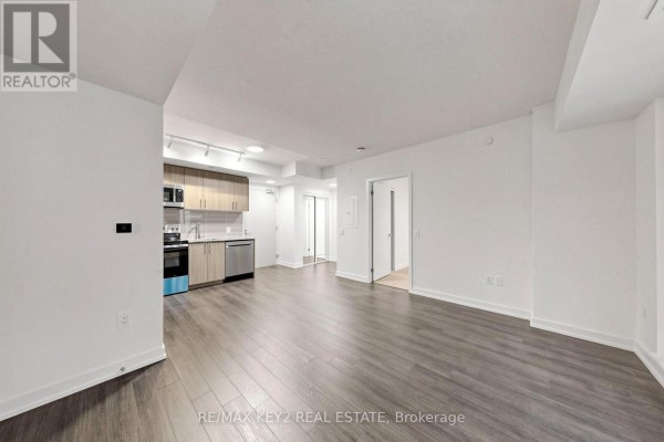 View of the open living space, kitchen area with stainless steel appliances, and a hallway leading to rooms. - 206 - 4010 Eglinton Avenue W, Toronto