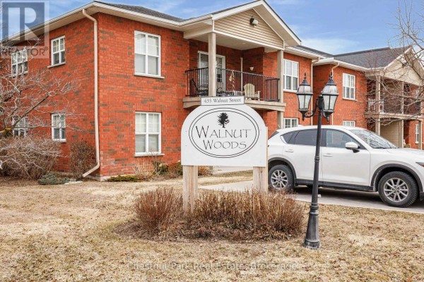 Close-up of 'Walnut Woods' sign with apartment building and white SUV. - 206 - 435 Walnut Street, Collingwood