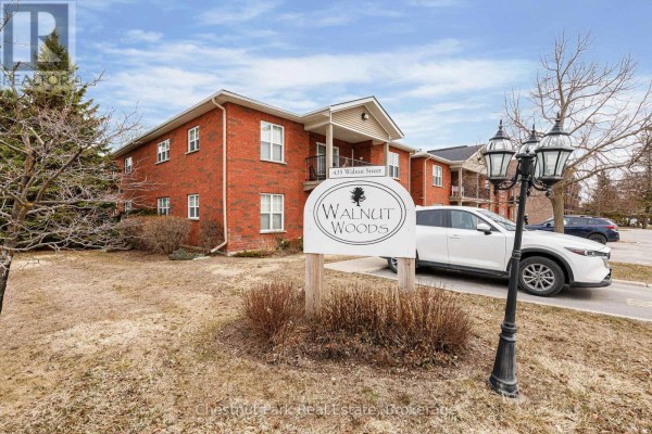Close-up of 'Walnut Woods' sign with apartment building and parked cars. - 206 - 435 Walnut Street, Collingwood
