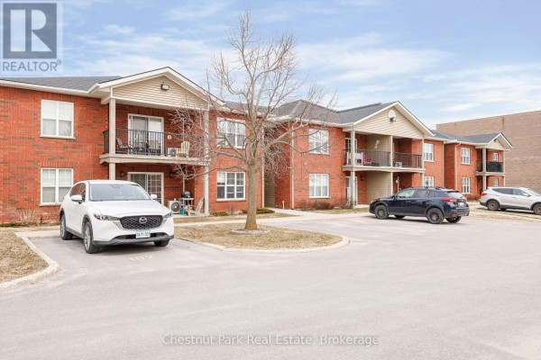 Exterior view of brick apartment building with parking lot and trees. - 206 - 435 Walnut Street, Collingwood