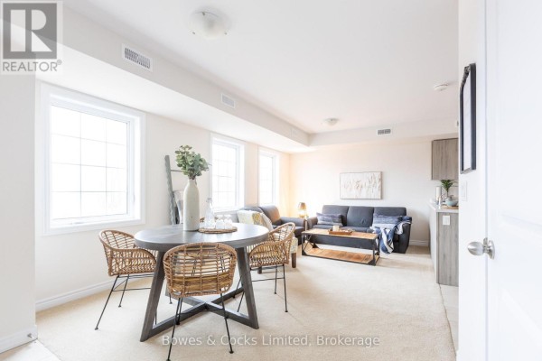 Open concept living and dining area with beige carpet, grey sofa, and large windows. - 206 - 48 Maple Avenue, Asphodel Norwood