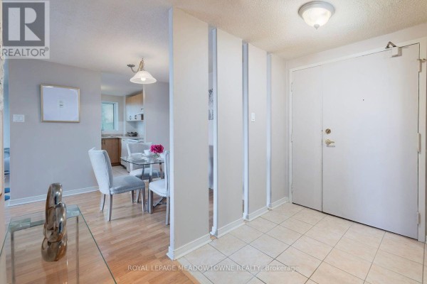 Foyer with tiled floor, beige walls, a white door, and a glimpse of a dining area. - 206 - 6720 Glen Erin Drive, Mississauga