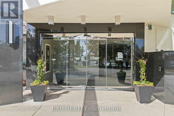 Modern building entrance with automatic glass doors, black stone accents, and potted plants. - 206 - 7250 Yonge Street, Vaughan