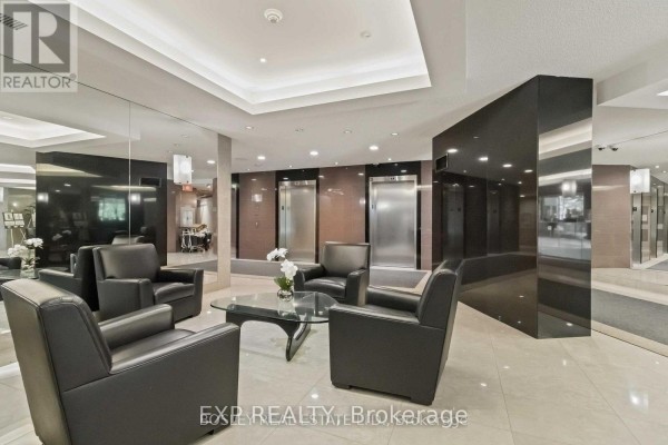 Building lobby with beige tiled floors, black leather armchairs, a glass coffee table, and elevators. - 206 - 7250 Yonge Street, Vaughan
