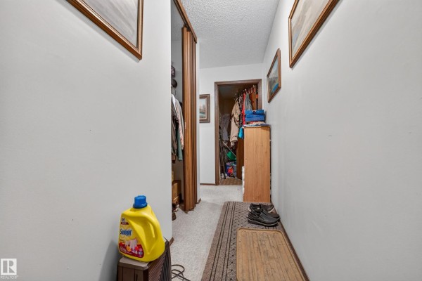 Narrow hallway with white walls, closet with folded clothes, wood door, and shoe rack. - #206 10842 107 St Nw, Edmonton