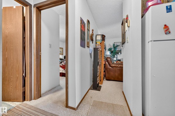Hallway with open doors to rooms, white walls, shelves, brown leather sofa, and refrigerator. - #206 10842 107 St Nw, Edmonton