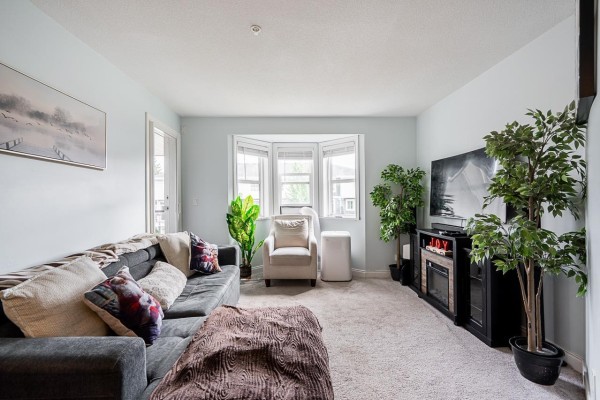 Living room and open kitchen area with hardwood floors and dining table. - 206 19774 56 Avenue, Langley