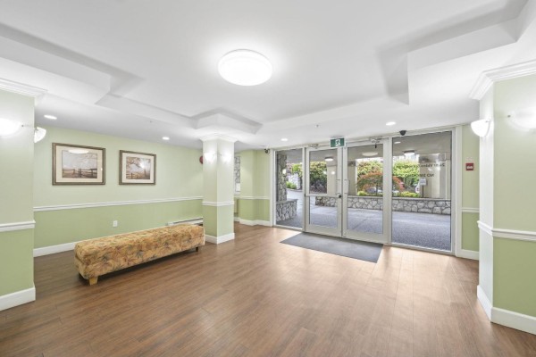 Interior hallway with light grey walls, wood floor, white doors, and red door. - 206 20120 56 Avenue, Langley