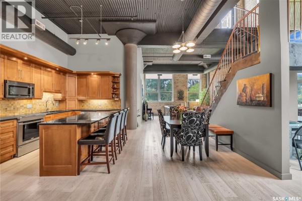 Open concept kitchen and dining area with light wood floors, wooden cabinets, and a black granite island. - 206 211 D Avenue N, Saskatoon
