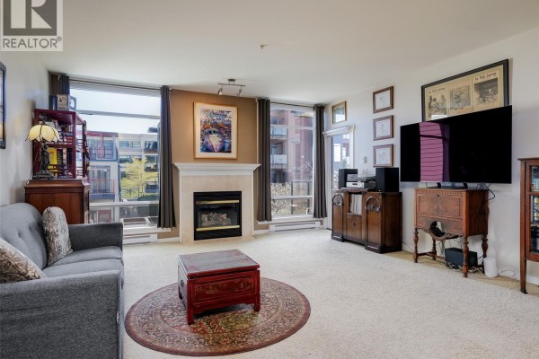 Living room with a sofa, dining area, and kitchen with blue cabinets. - 206 330 Waterfront Cres, Victoria