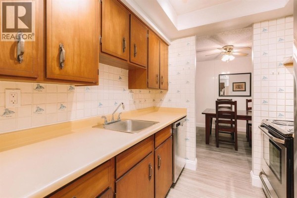 Long apartment kitchen with wood cabinets, stainless steel appliances, and sink. - 206 410 Agnes Street, New Westminster
