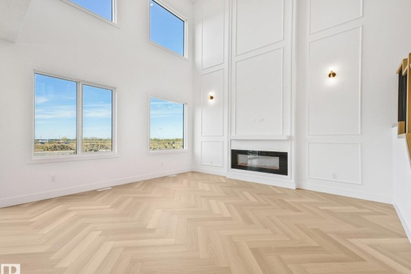 Living room with high ceilings, large windows, a modern fireplace, and light wood herringbone floors. - 206 Corral Circle, Sherwood Park