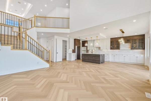 Spacious open-plan living area with a grand staircase, kitchen, and dining space with herringbone floors. - 206 Corral Circle, Sherwood Park