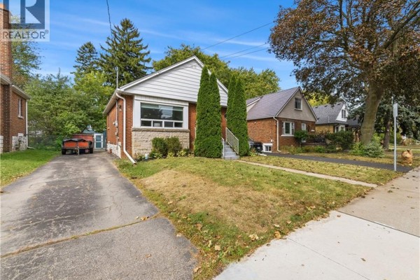 Side exterior view of the brick bungalow with a driveway and adjacent properties. - 206 East 19th Street, Hamilton