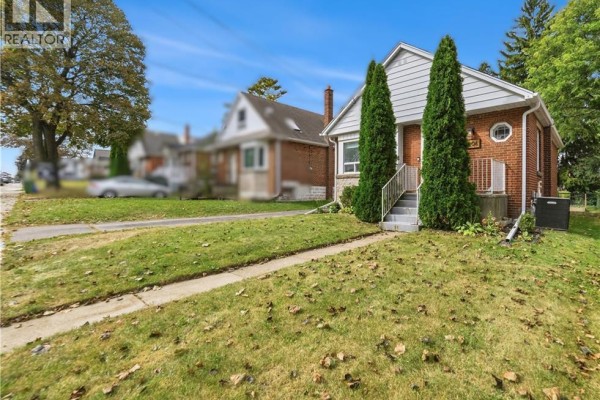 View of the bungalow from the side yard showing green grass and mature trees. - 206 East 19th Street, Hamilton