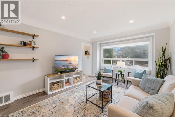 Living room with a sofa, coffee table, television, and a large window with natural light. - 206 East 19th Street, Hamilton