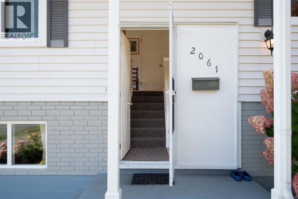 Open front door revealing a carpeted staircase leading upwards, with house number 2061 displayed. - 2061 Forest Dr, Nanaimo