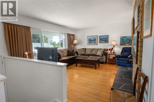 Living room with a fireplace, large windows, sofas, a coffee table, and wood flooring. - 2061 Forest Dr, Nanaimo