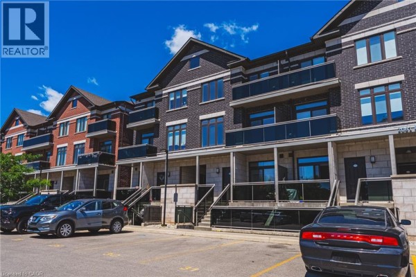 Townhouse exterior with brick facade, balconies, and paved parking lot with cars. - 2061 Prospect Street Unit# 211, Burlington