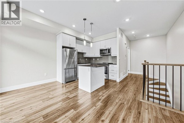 Open-concept living area with white cabinets, stainless steel appliances, and wood flooring. - 2061 Prospect Street Unit# 211, Burlington
