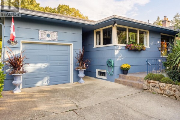 Light blue siding, attached garage, and concrete driveway with potted plants. - 2064 Lansdowne Rd, Oak Bay