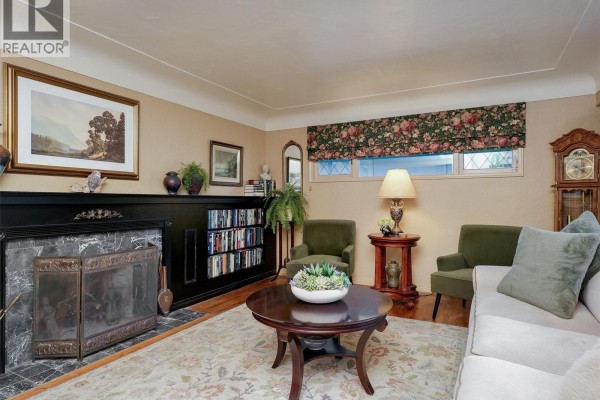 Living room with fireplace, built-in bookshelves, armchair, and coffee table. - 2064 Lansdowne Rd, Oak Bay