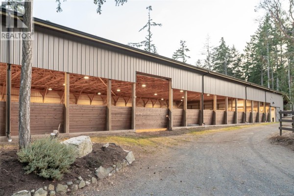 Exterior of a large metal barn with stables and horse stalls visible inside. - 2065 Sanders Rd, Nanoose Bay