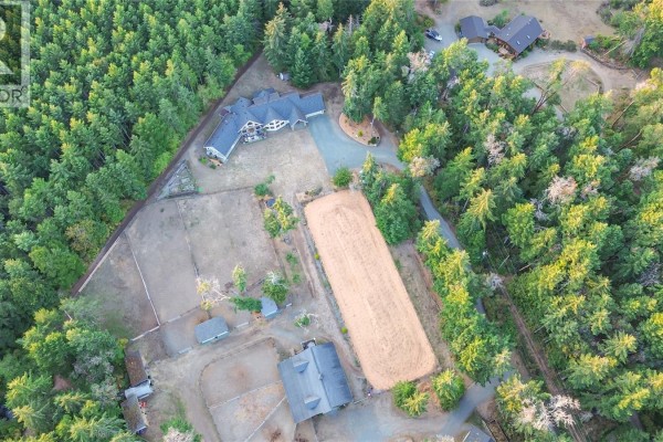 Overhead view of a property with a large house, stables, riding arena, and surrounding woodland. - 2065 Sanders Rd, Nanoose Bay
