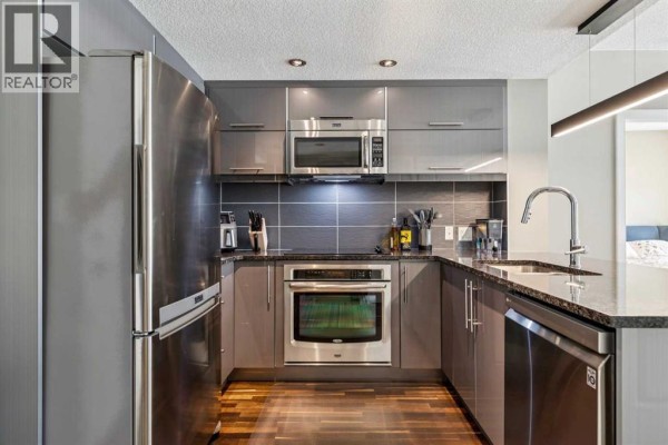 Kitchen with grey cabinets, stainless steel appliances, and a large stainless steel refrigerator. - 207, 1110 3 Avenue Nw, Calgary