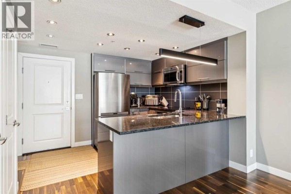 View of a modern kitchen with grey cabinets and a doorway to another room. - 207, 1110 3 Avenue Nw, Calgary