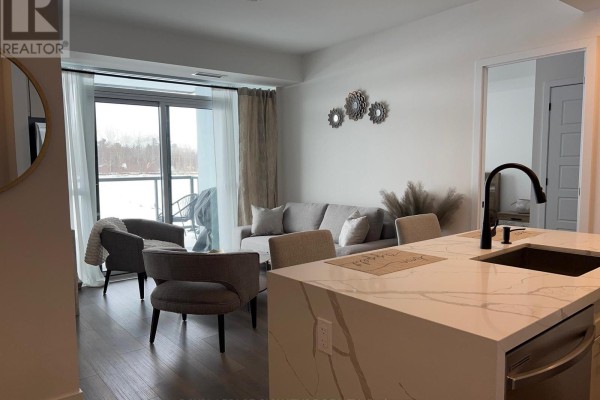 Open concept living and kitchen area with grey furniture and a large marble island. - 207 - 415 Sea Ray Avenue, Innisfil