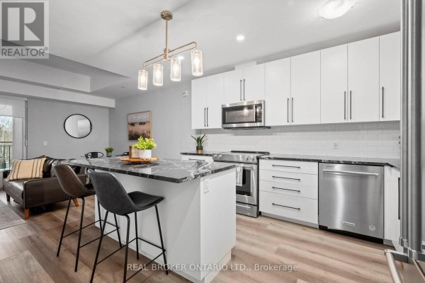 Kitchen island with seating, white cabinets, and a view of a living room area. - 207 - 51 David Street, Kitchener