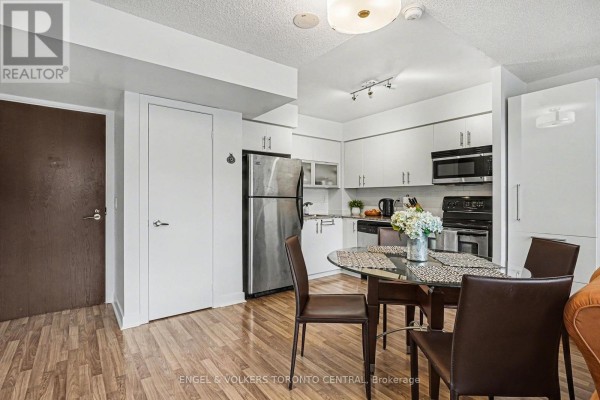 Kitchen area with white cabinets, stainless steel appliances, and a glass-top dining table. - 207 - 80 Western Battery Road, Toronto